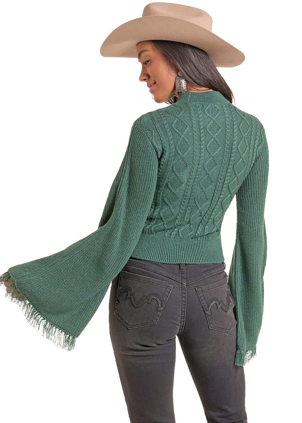 A woman shown from the back wearing a sage green knit sweater with long fringed bell sleeves, dark charcoal gray jeans, and a beige cowboy hat against a plain white background.