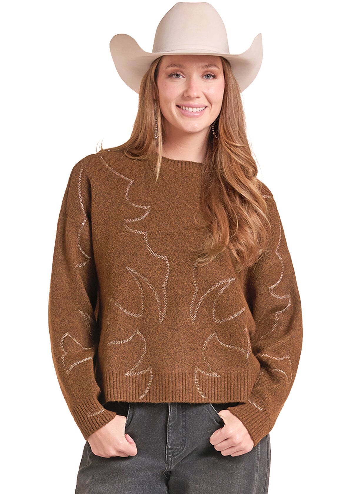 A woman wearing a brown knit sweater with a light beige leaf pattern, paired with a beige cowboy hat and dark gray jeans, against a plain white background.