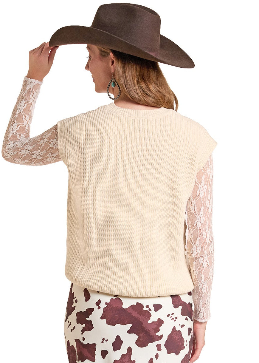 A woman shown from the back wearing a cream ribbed sleeveless sweater vest over a cream lace long-sleeve top, a brown-and-cream cow-print midi skirt, and brown cowboy boots, against a plain white background.