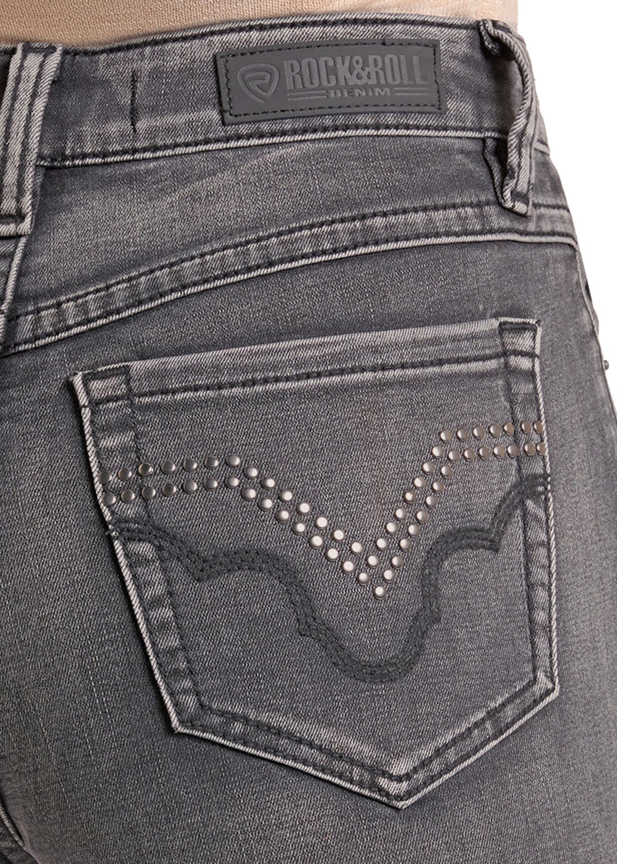 Close-up of the back pocket of dark gray denim jeans featuring a studded western-style wave design and a Rock & Roll brand patch on the waistband.