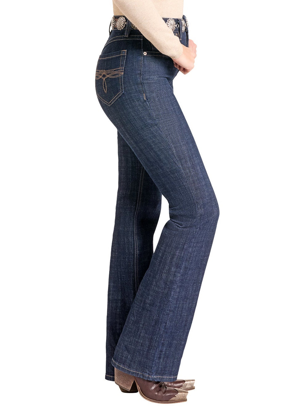 A woman modeling dark blue flare jeans with a western-style belt, paired with a cream long-sleeve top, brown boots, and a black cowboy hat, shown from a side profile against a white background.