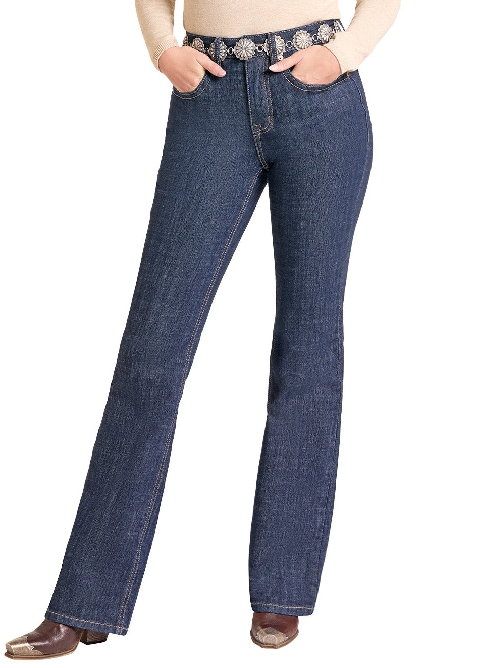 A woman modeling dark blue flare jeans with a western belt, a beige long-sleeve top, and a black cowboy hat against a white background.