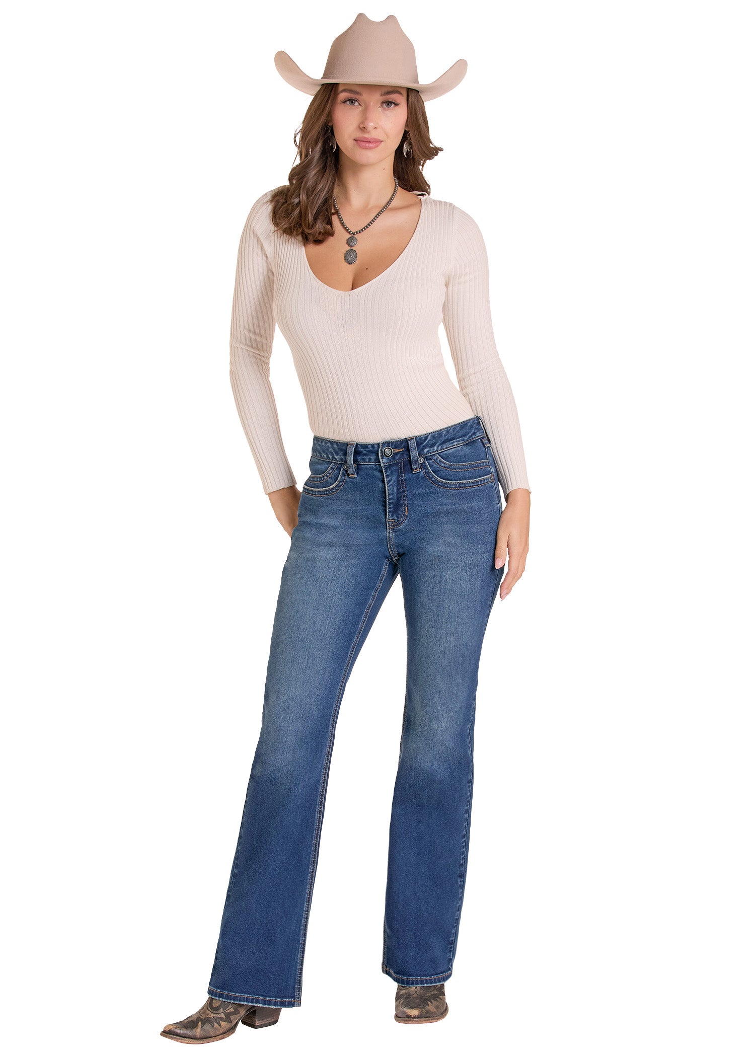 A woman modeling blue flare jeans with a cream ribbed long-sleeve top, a beige cowboy hat, and brown cowboy boots against a plain white background.