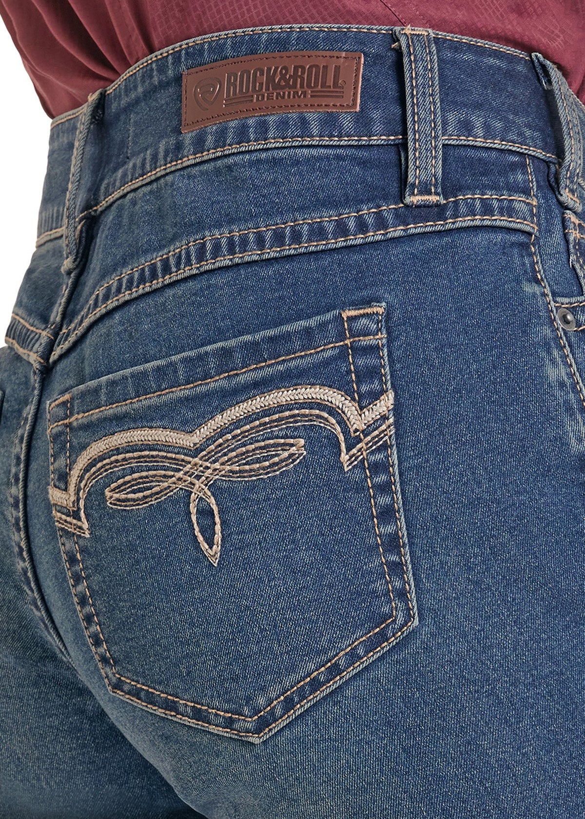 Close-up of the back waistband and pocket area of blue denim jeans, showing a brown Rock & Roll brand patch at the back waist and decorative white contrast stitching on the pocket.