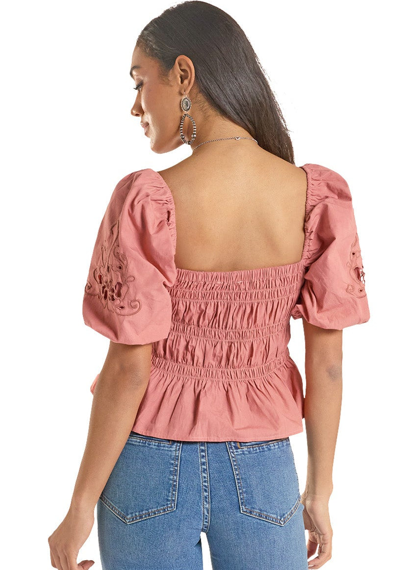 Woman wearing a pink blouse with puff sleeves and blue jeans on a white background