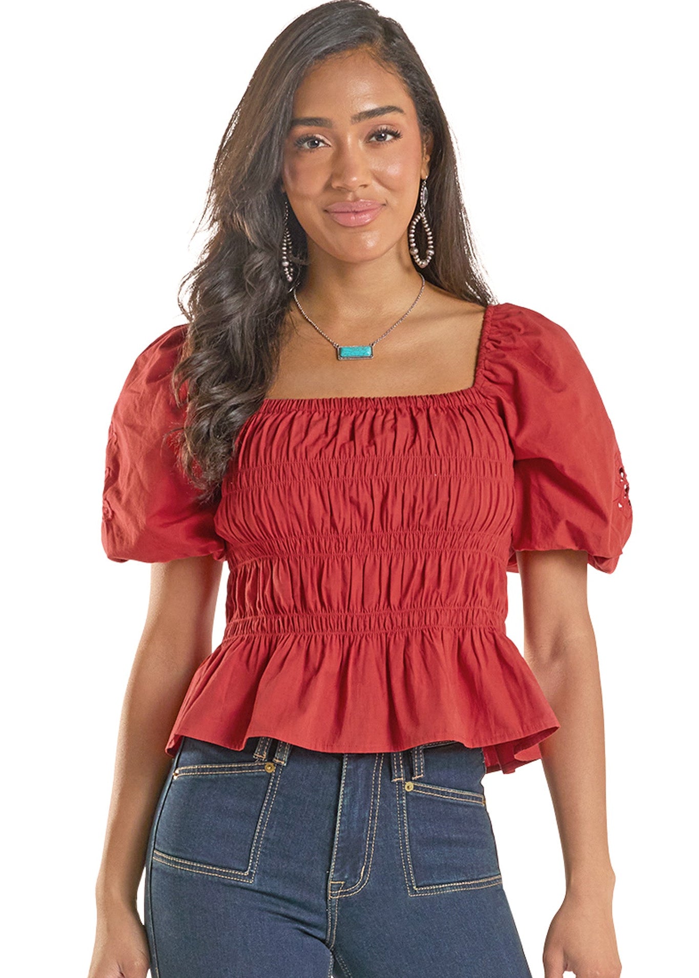Woman wearing a red top with puff sleeves and blue jeans on a white background