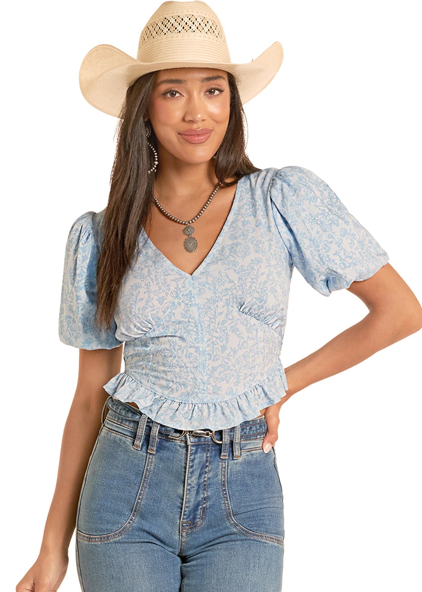 Woman wearing a blue patterned top and jeans with a beige cowboy hat on a white background