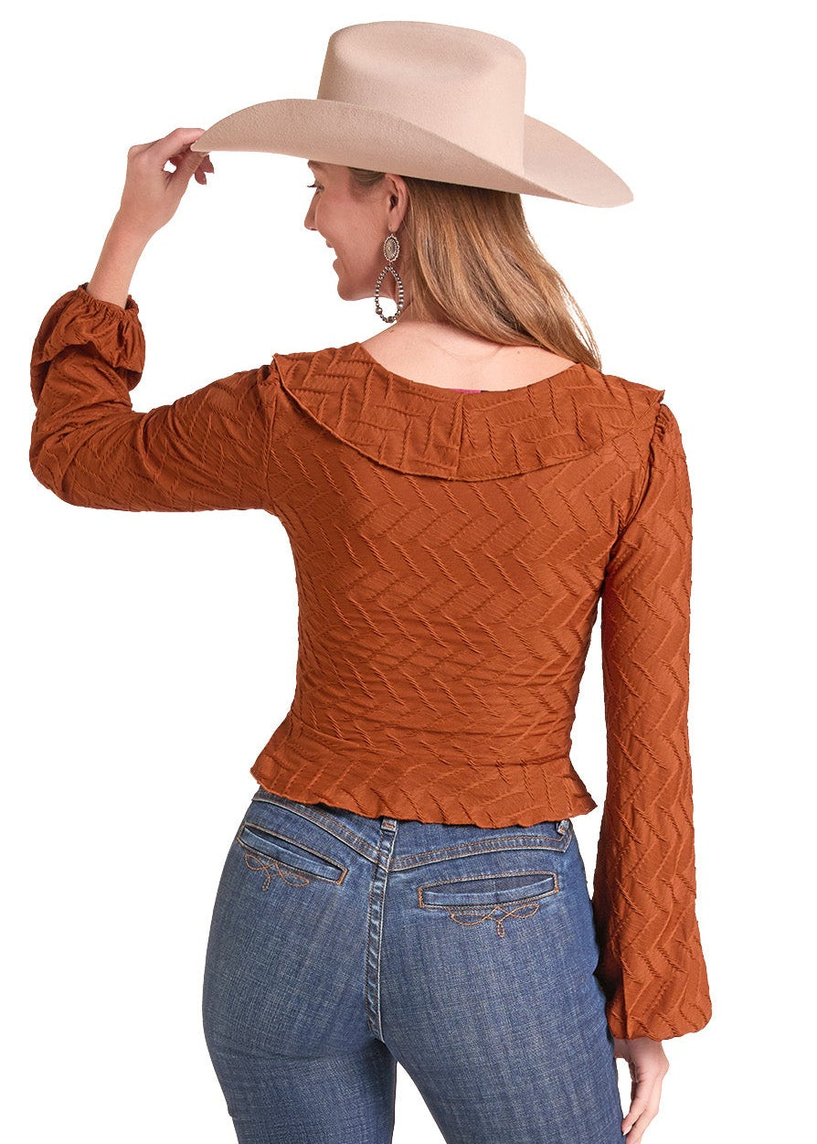 A woman shown from the back wearing a fitted rust-orange textured long-sleeve top, blue jeans, and a beige cowboy hat.