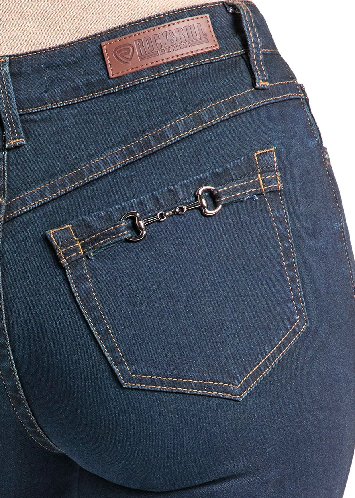 Close-up rear view of dark blue denim jeans on a model, showing the back pocket with a decorative metal ring detail and a brown leather brand patch at the waistband.