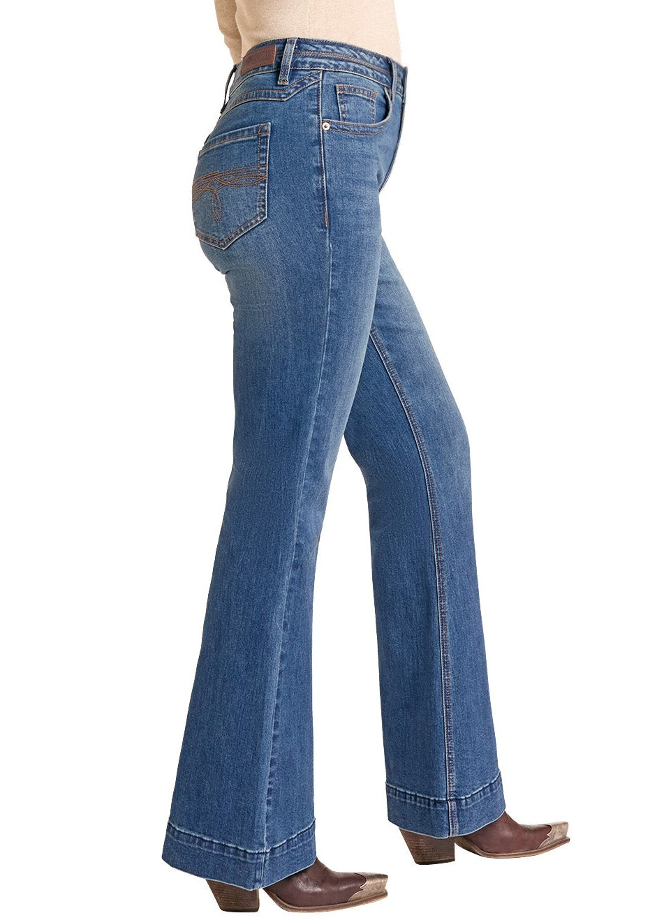 A woman wearing a beige cowboy hat, beige long-sleeve top, blue flare jeans, and brown cowboy boots, shown in profile against a plain white background.