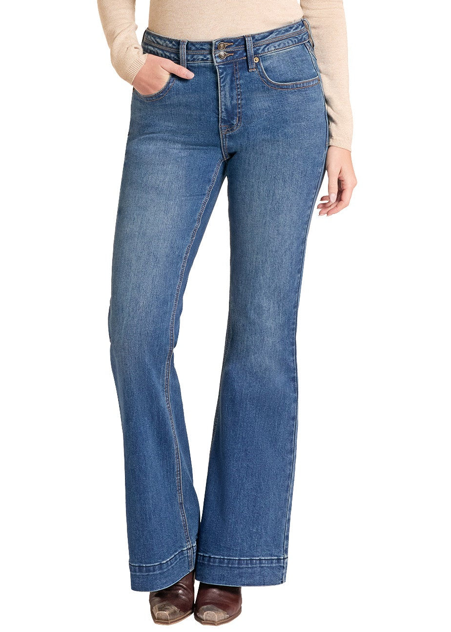 A woman modeling a beige long-sleeve top, blue flare jeans, and a tan cowboy hat against a plain white background.