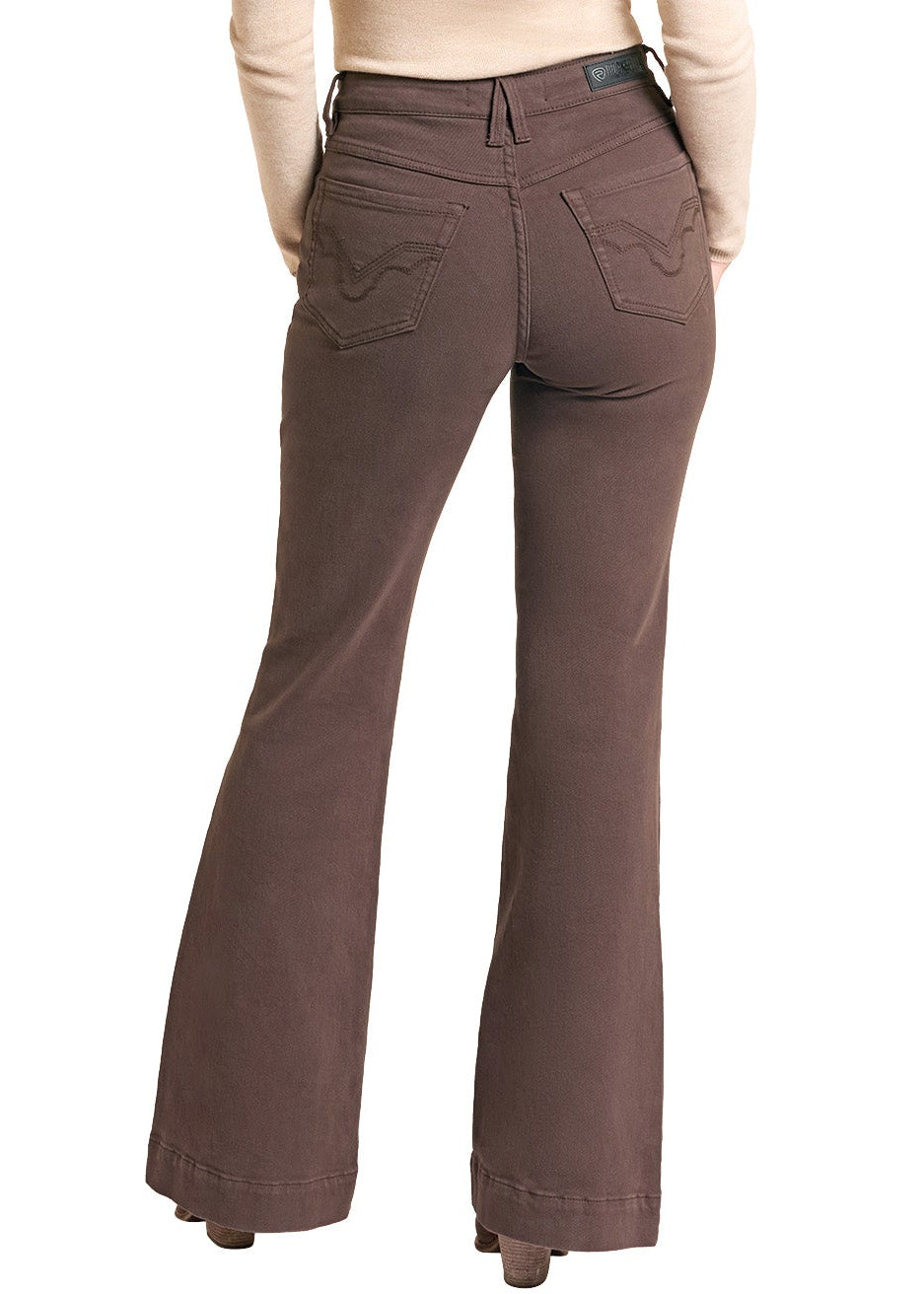 A woman shown from the back wearing brown flared pants, a beige long-sleeve top, and a brown cowboy hat against a plain white background.