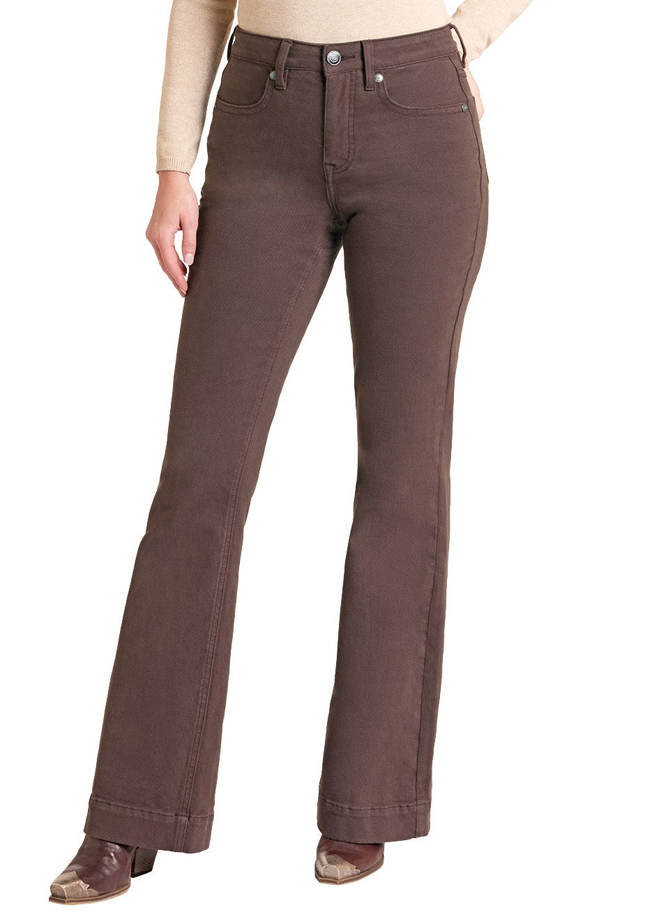 A woman modeling a pair of dark brown bootcut jeans with a beige long-sleeve top, a brown cowboy hat, and brown cowboy boots against a plain white background.