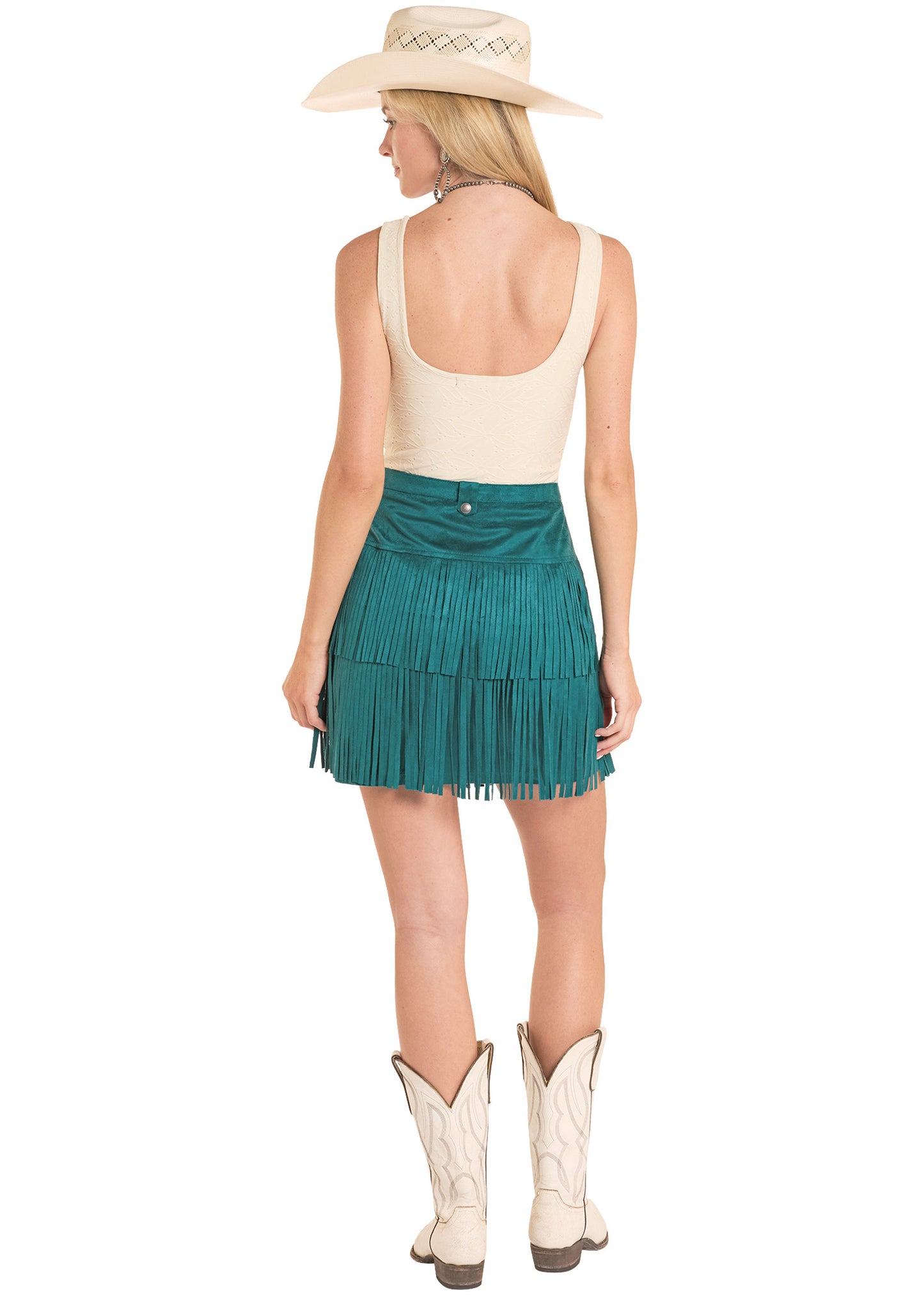 Woman wearing a green fringe skirt, cream top, and white cowboy boots on a white background