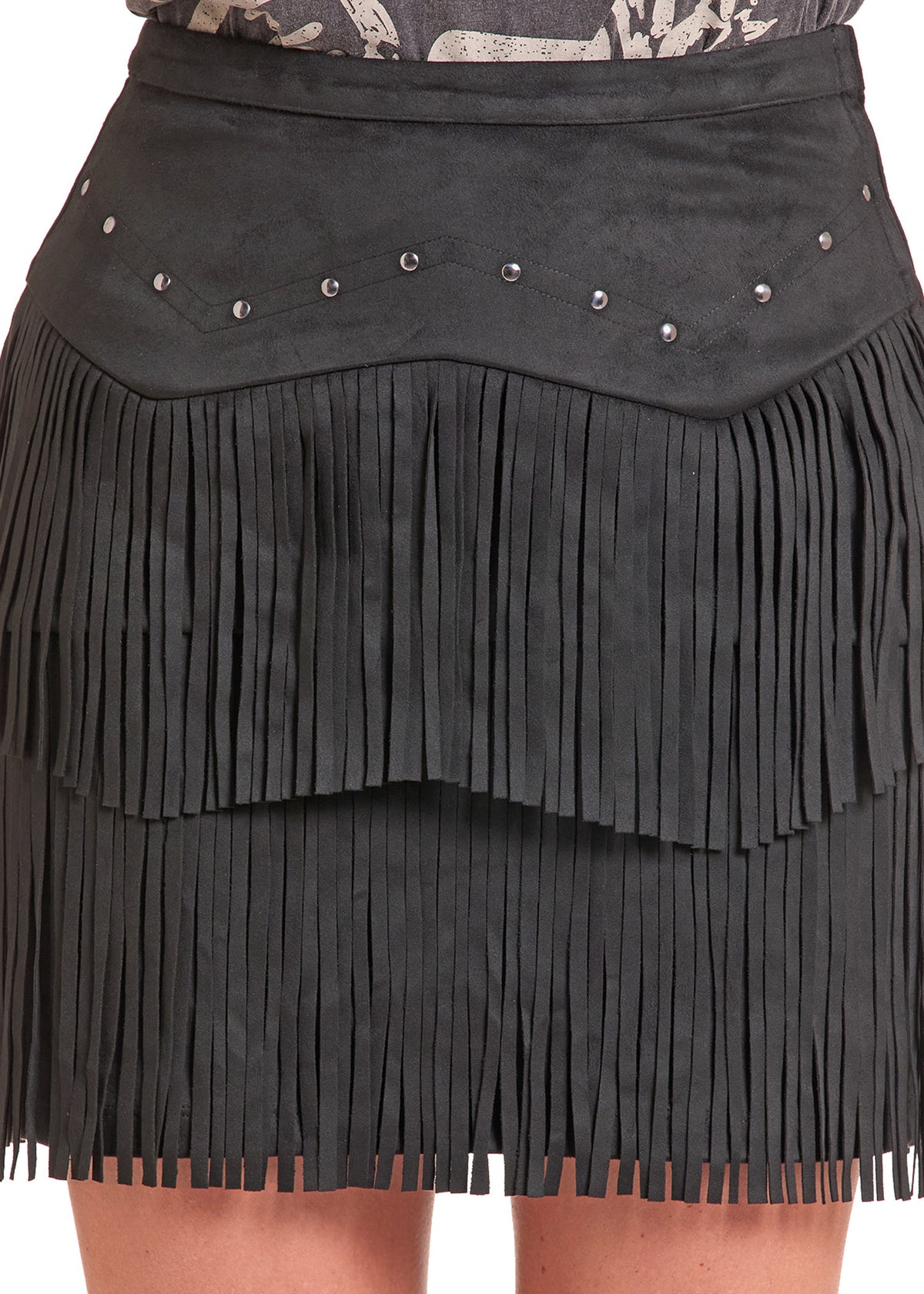 Close-up of a black faux-suede fringe skirt with silver-tone metal studs on the waistband, worn with a patterned top and bare legs visible.
