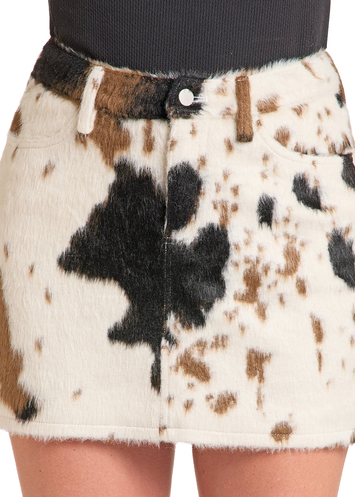 A close-up of a faux fur mini skirt with a cow print pattern in black, brown, and cream, featuring a dark brown faux fur belt with a silver button closure.