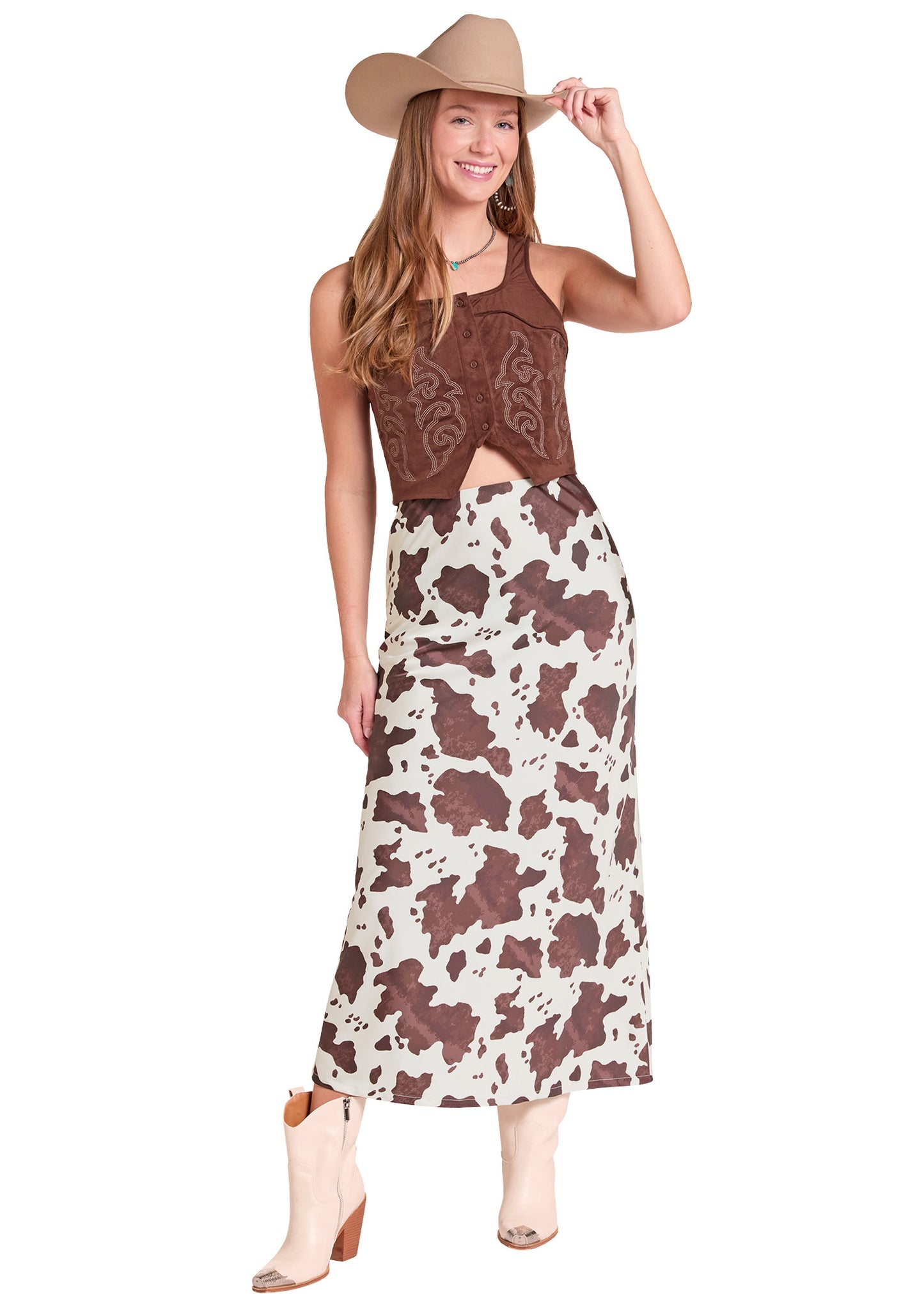 A woman modeling a two-piece western outfit consisting of a brown embroidered sleeveless crop top and a brown and cream cow-print maxi skirt.
