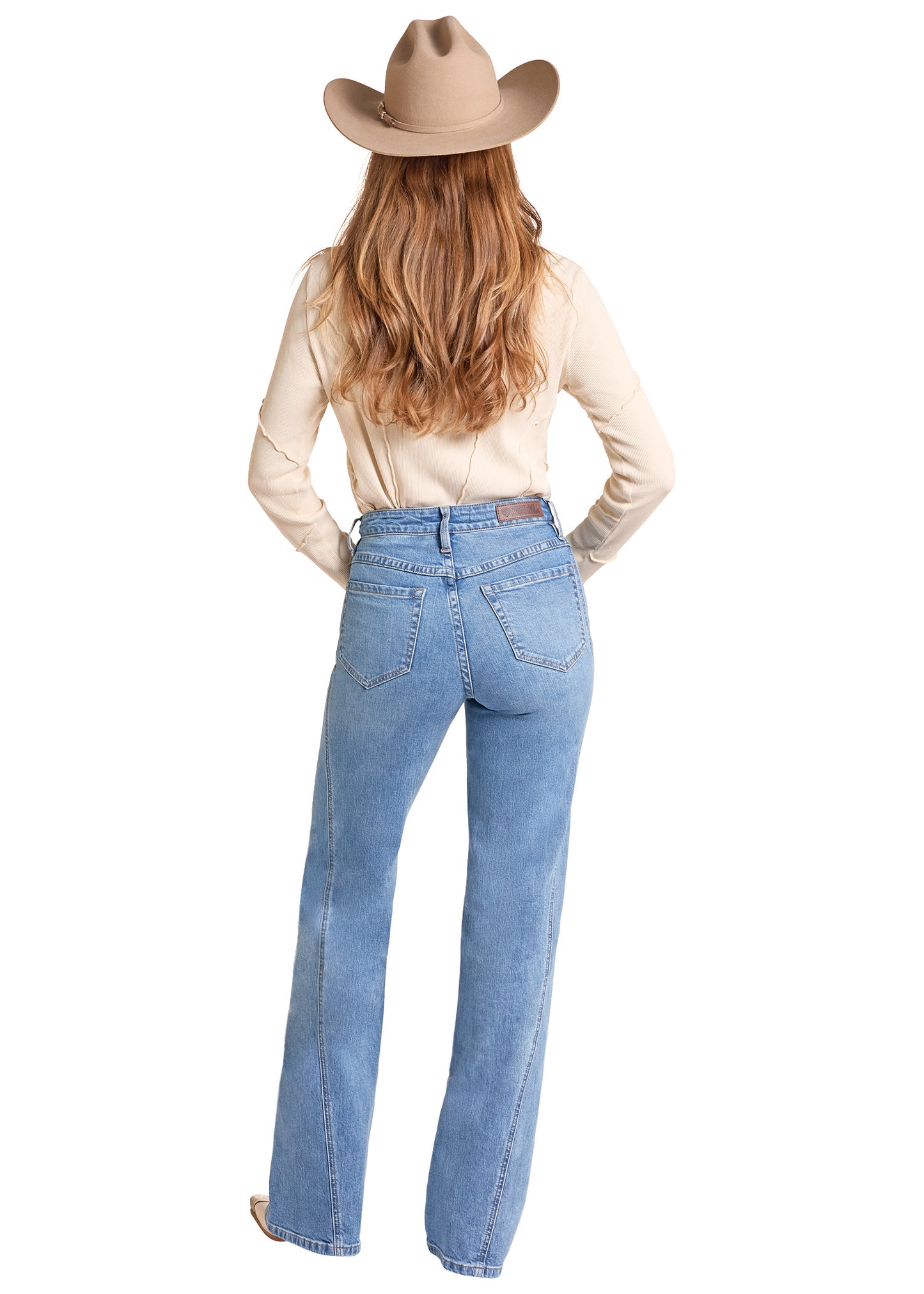 A woman shown from the back wearing a tan cowboy hat, a cream long-sleeve top, and light blue high-waisted flare jeans against a plain white background.