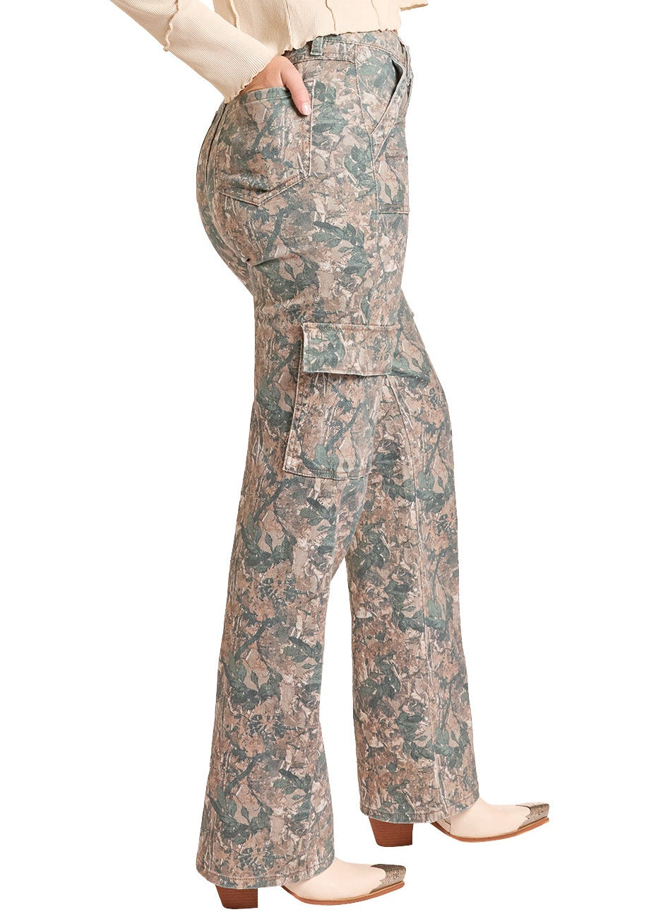 A woman modeling a western outfit consisting of a light beige long-sleeve shirt, a tan cowboy hat, and high-waisted camouflage cargo flare pants, posed against a solid white background.