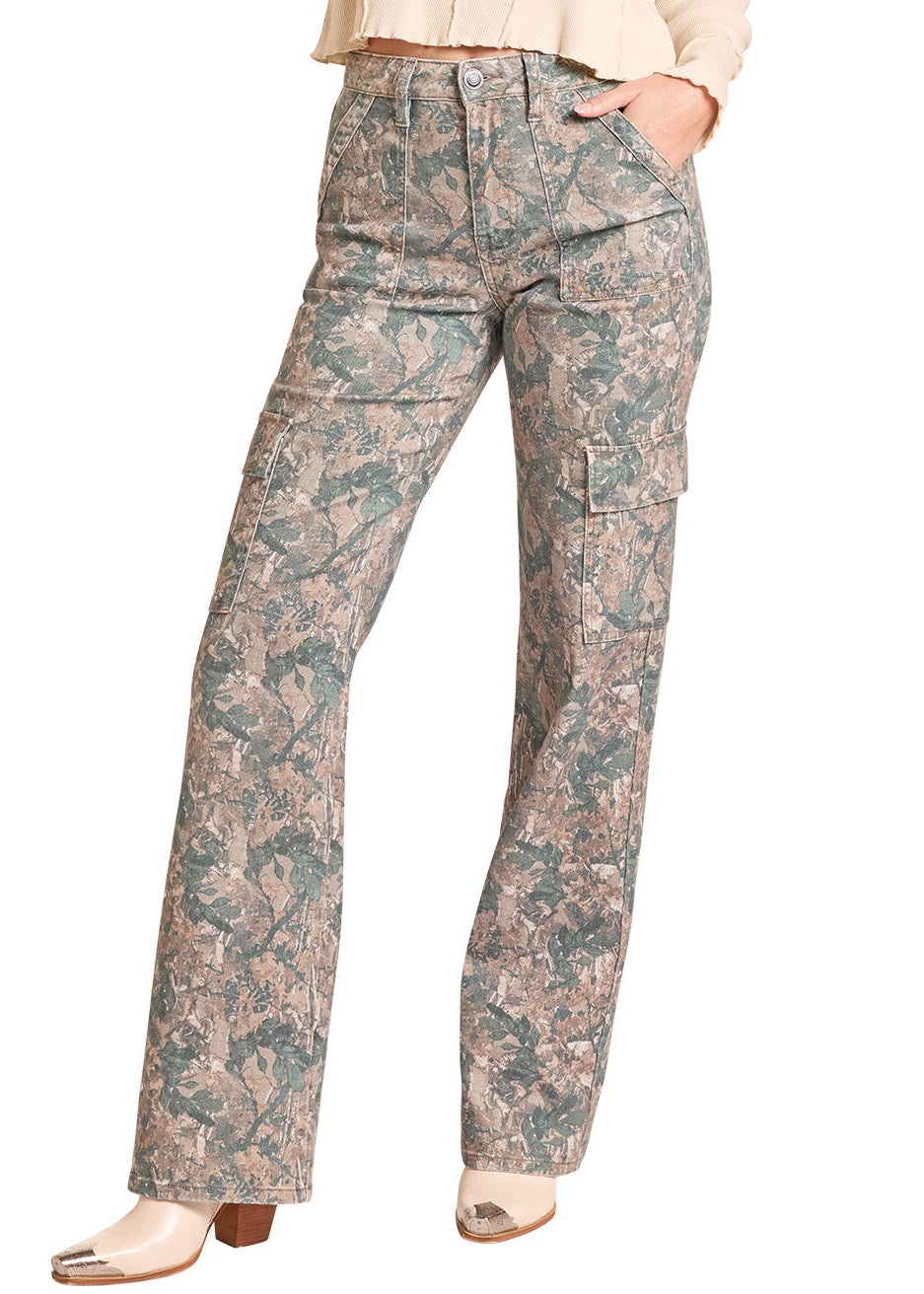 A woman modeling a western outfit consisting of a beige long-sleeve cropped top, a tan cowboy hat, and high-waisted patterned pants in beige, green, and blue tones, set against a plain white background.
