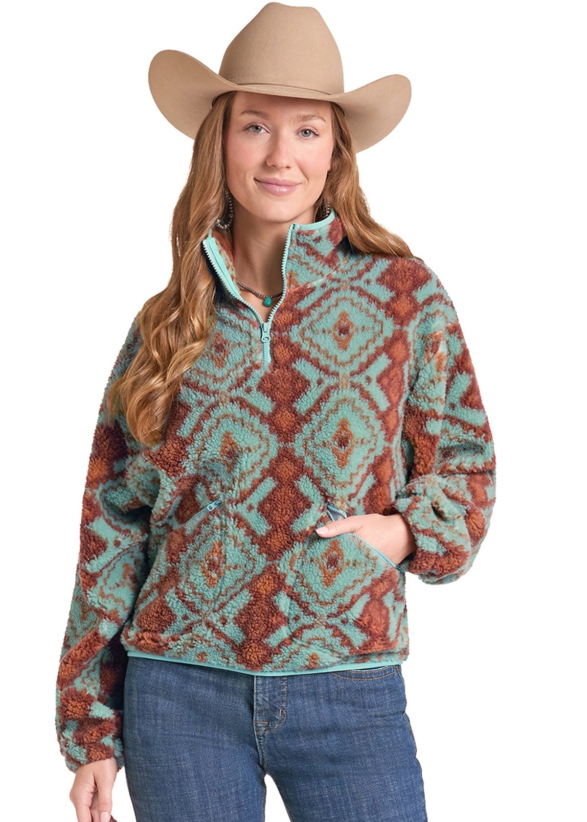 A woman wearing a tan cowboy hat and a long-sleeve quarter-zip fleece pullover with a rust brown and turquoise geometric pattern, paired with blue jeans, against a plain white background.