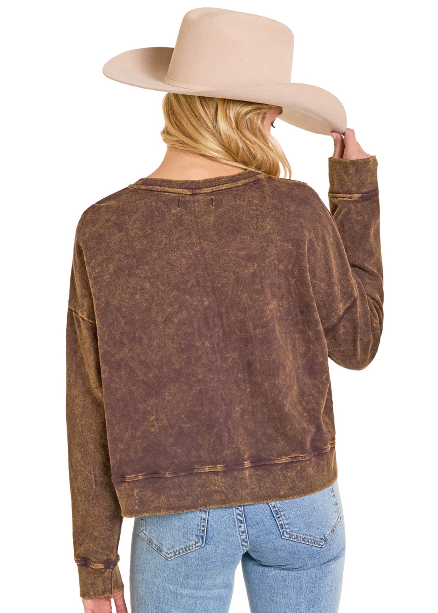 Person wearing a brown distressed sweatshirt and blue jeans with a beige hat on a white background