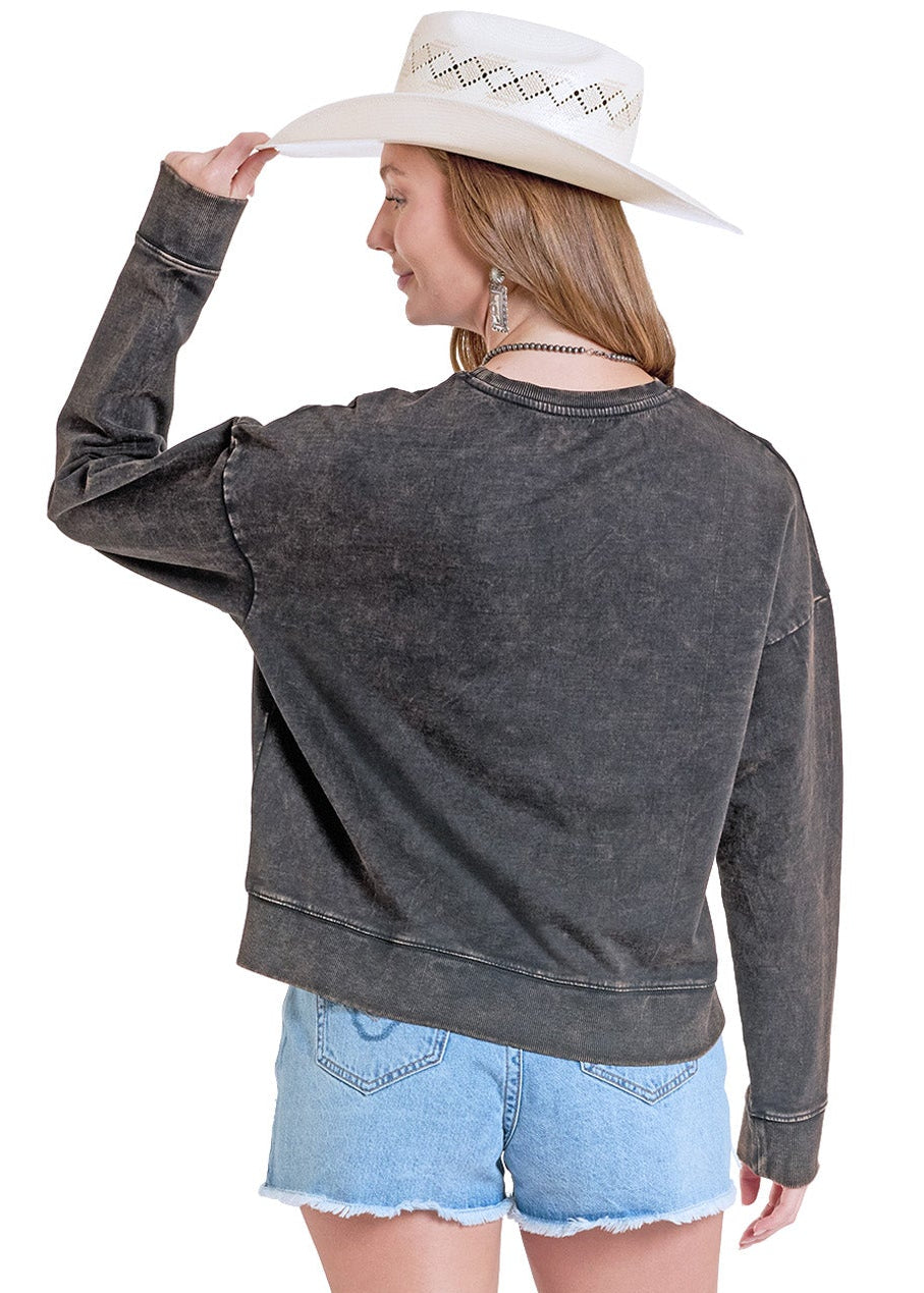 the back of a woman wearing a acid washed crewneck with a cowboy hat.