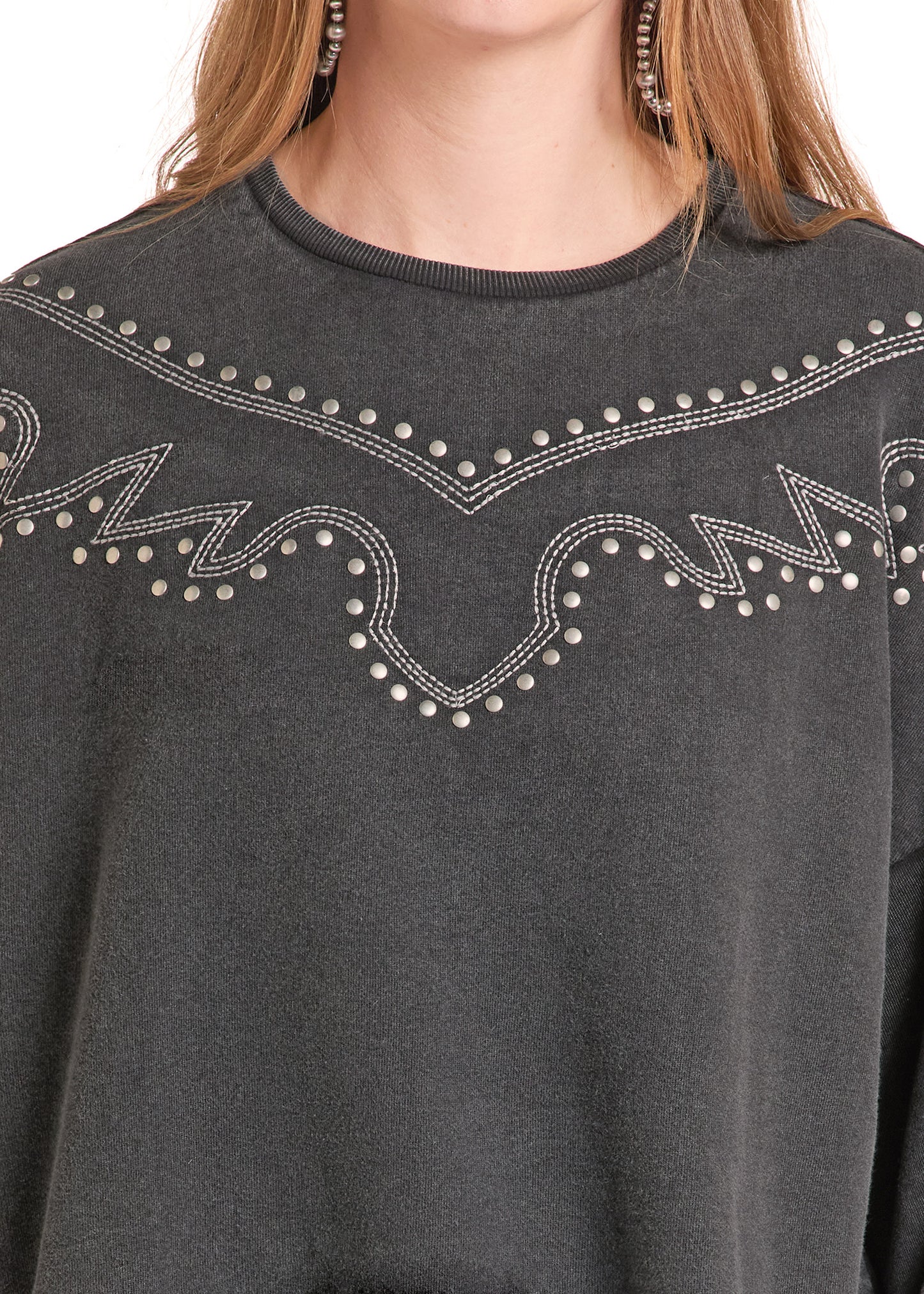 Close-up of a dark gray crewneck sweatshirt featuring western-style silver rhinestone embroidery across the chest, worn by a model.