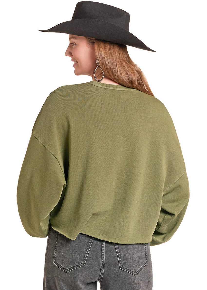 A woman shown from the back wearing an olive green cropped long-sleeve sweater, dark gray wide-leg jeans, a black wide-brim hat, and black boots, against a plain white background.