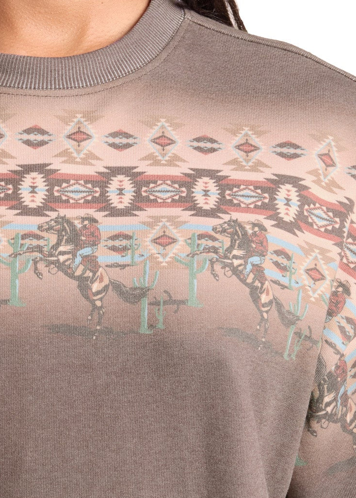 A woman wearing a taupe-brown crewneck sweatshirt with a faded geometric and Native American-inspired pattern across the chest and shoulders.