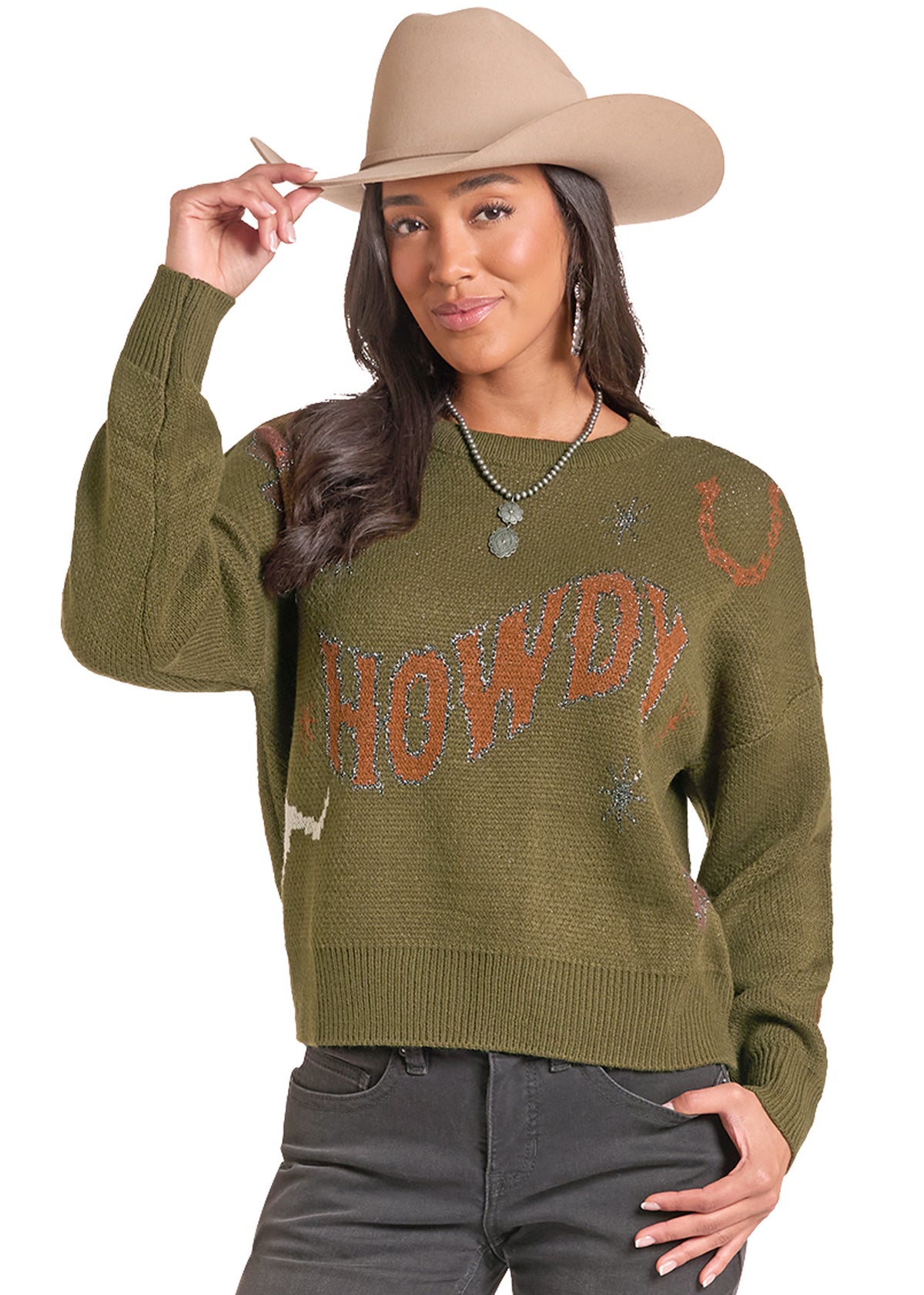 A woman wearing an olive green knit sweater with 'HOWDY' and western motifs, paired with a tan cowboy hat and dark gray jeans, against a plain white background.
