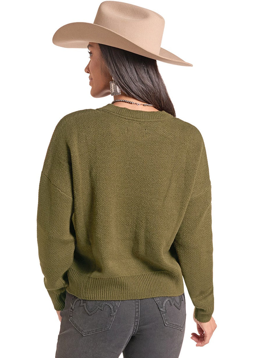 A woman shown from the back wearing an olive green knit sweater, dark gray jeans, and a beige cowboy hat against a plain white background.
