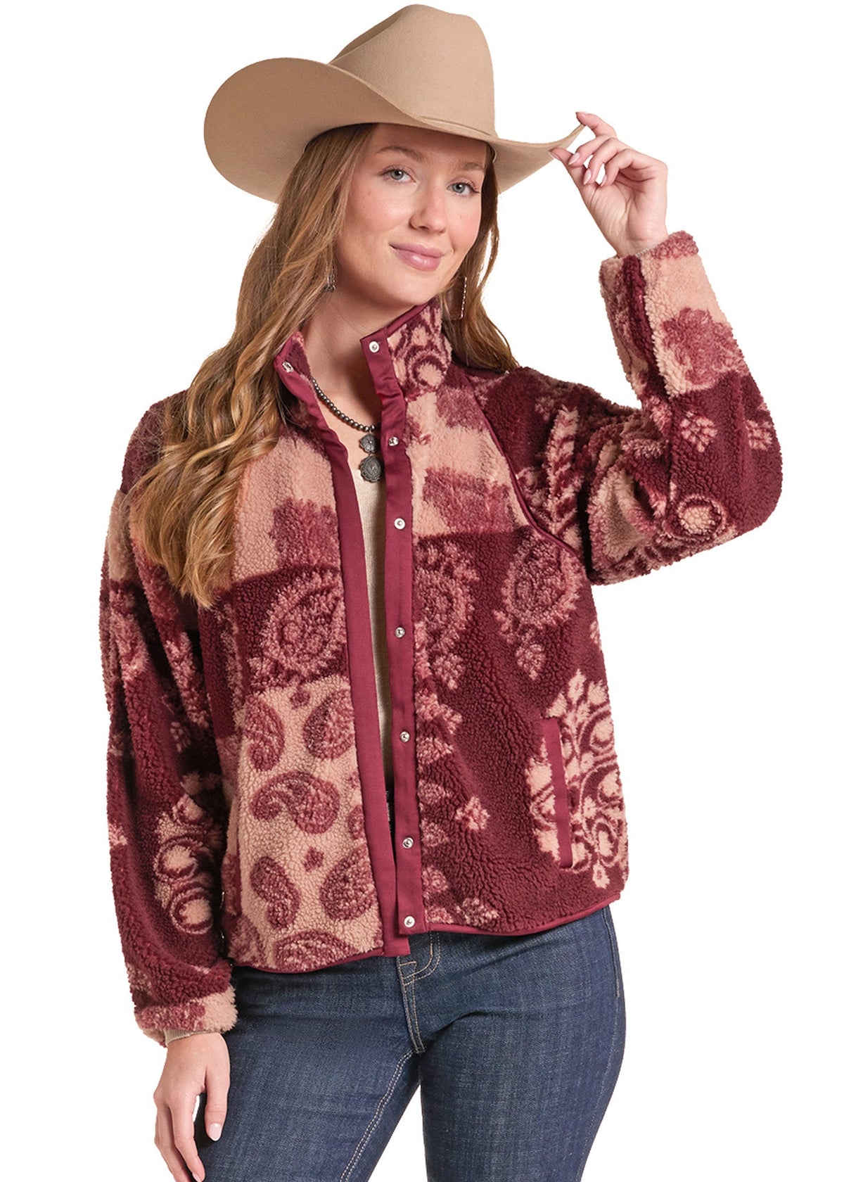 A woman wearing a  patterned sherpa fleece jacket, a tan cowboy hat, and blue jeans, posing against a white background.