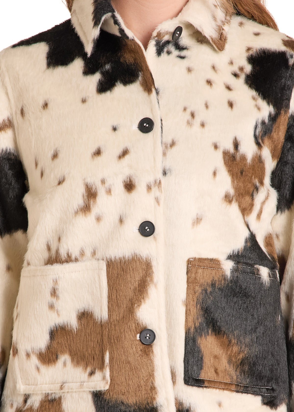 Close-up of a faux-fur button-front jacket with a cowhide-inspired pattern in cream, brown, and black, showing the collar, front buttons, and patch pockets.