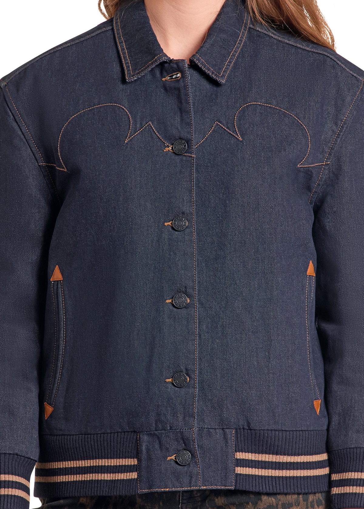 A close-up of a dark blue denim jacket with decorative contrast stitching, button closure, and striped ribbed cuffs and hem.