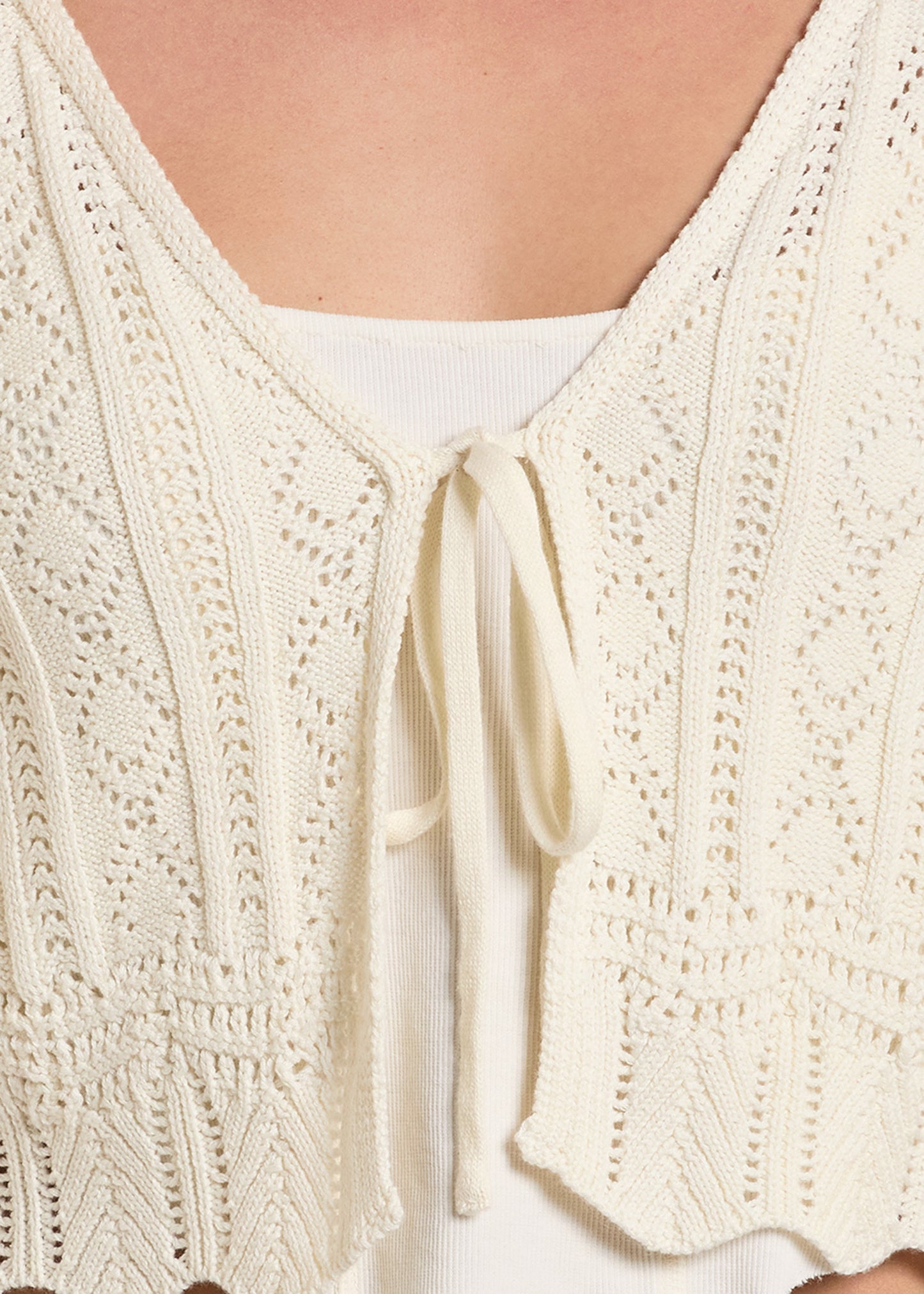 Close-up of a cream-colored knitted cardigan with a tie detail.