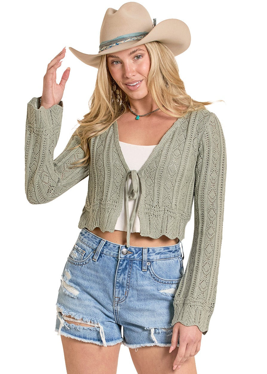 Woman wearing a green cardigan, denim shorts, beige boots, and a cowboy hat on a white background