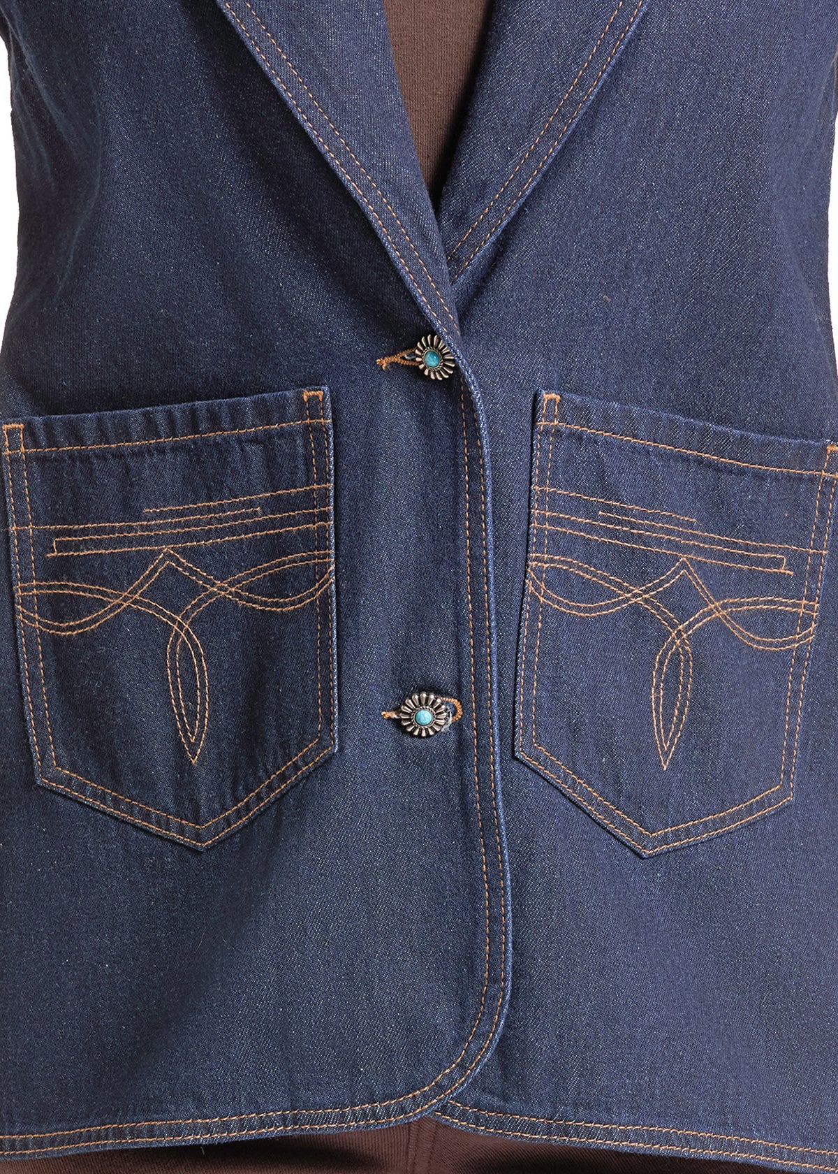 Close-up of a dark blue denim vest with decorative contrast stitching on the front pockets and two ornate turquoise-style buttons.