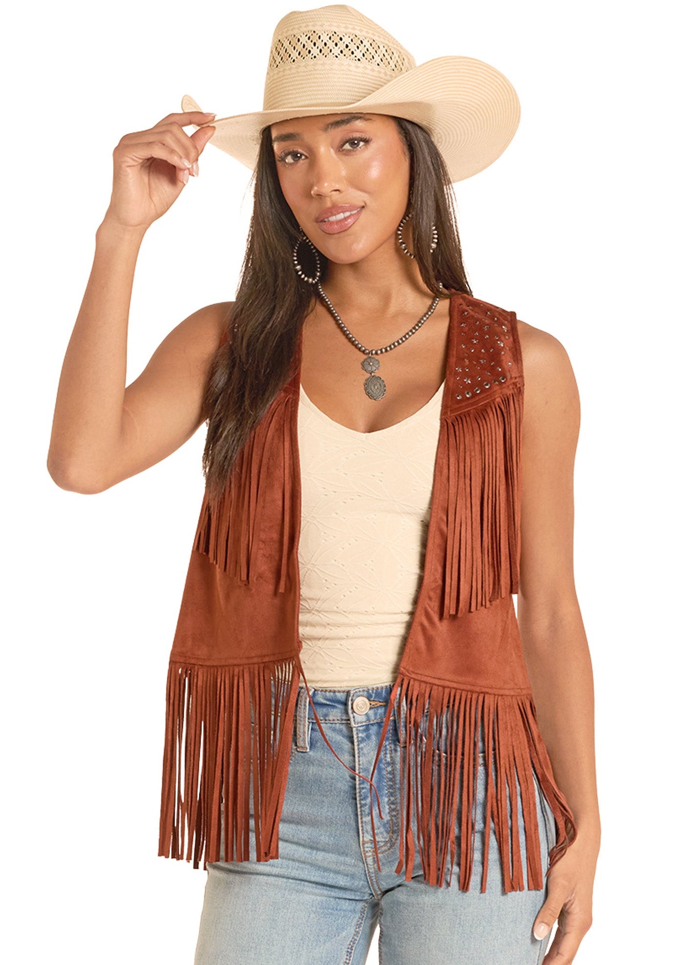 Woman wearing a brown fringe vest, beige top, and jeans with a white background