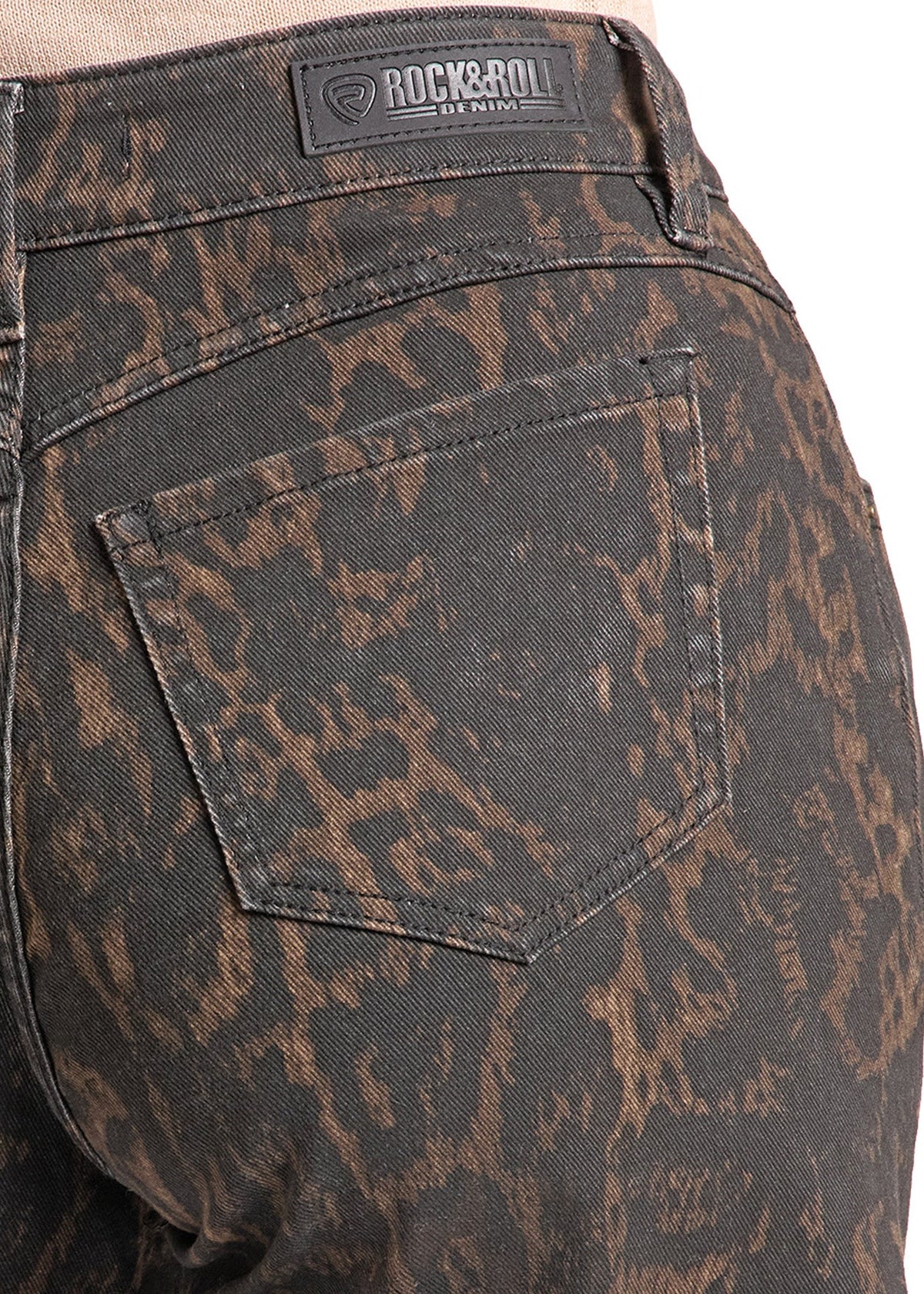 Close-up of the back waistband and pocket area of dark washed denim jeans with a brown abstract distressed pattern. A Rock & Roll brand patch is visible on the waistband.