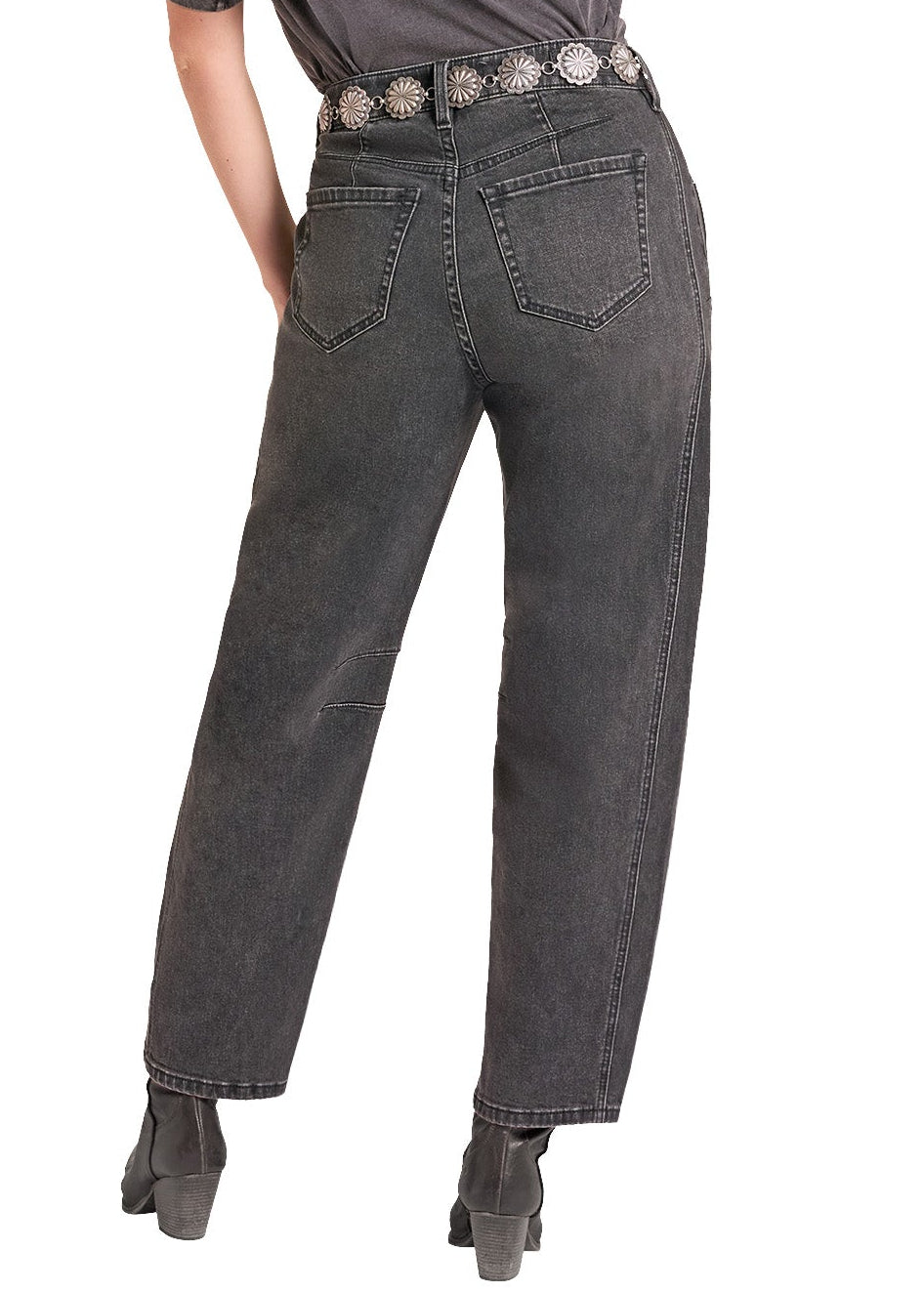 A woman shown from the back wearing a black cowboy hat, a dark gray t-shirt, dark gray high-waisted jeans with a silver concho belt, and black boots, set against a plain white background.