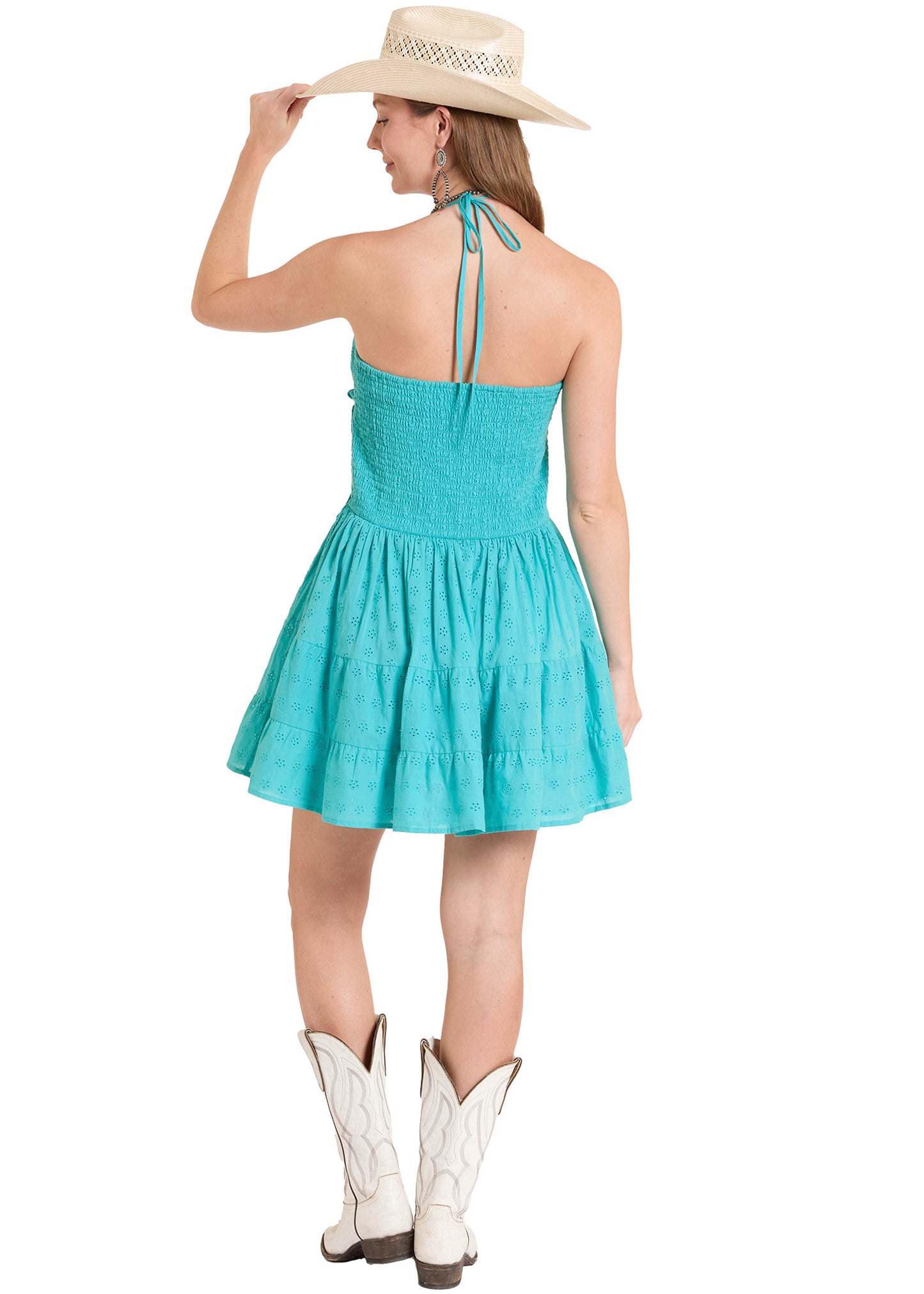 Woman wearing a turquoise dress, white cowboy boots, and a beige hat on a white background