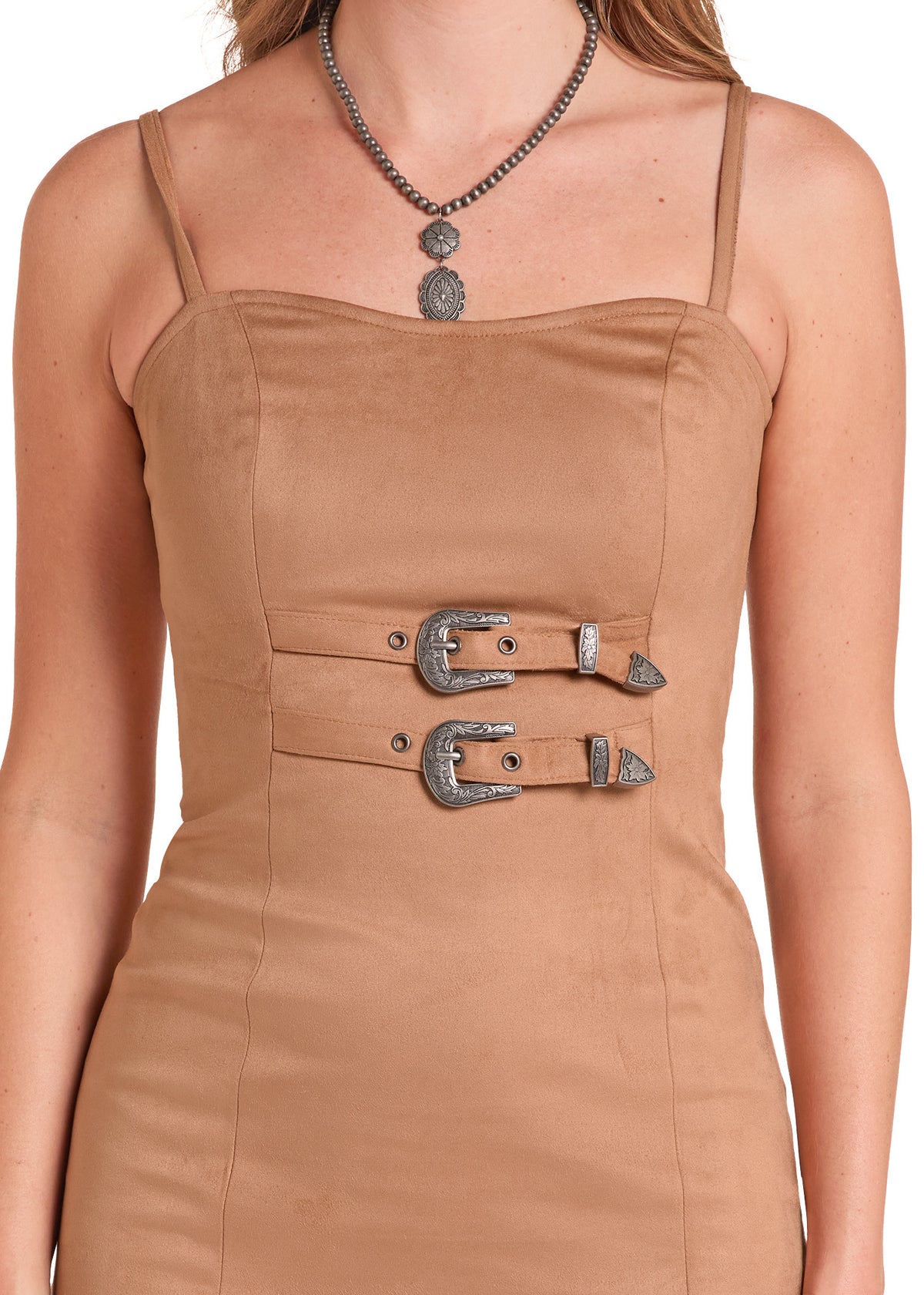 A close-up of a model wearing a tan faux-suede spaghetti-strap dress with double waist belts and silver buckle details, styled with a silver pendant necklace.