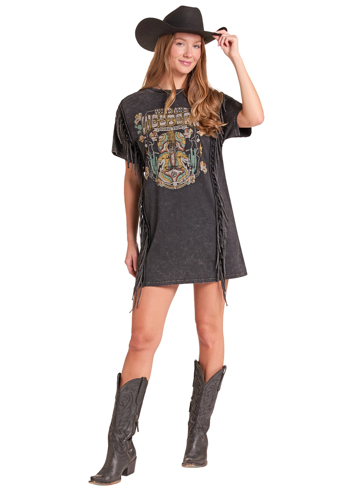 A woman modeling a black acid-wash fringed t-shirt dress with a western graphic print, styled with a black cowboy hat and dark brown leather cowboy boots against a white background.