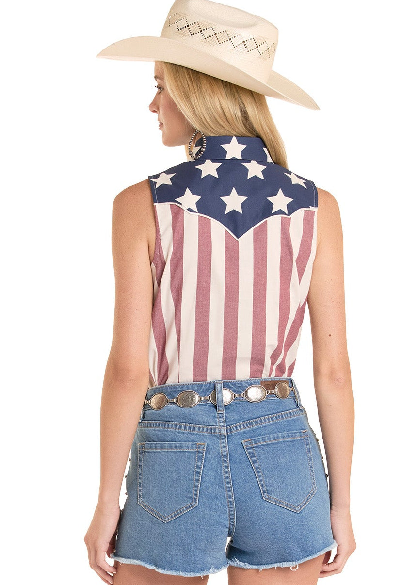 Woman wearing a sleeveless top with an American flag design, denim shorts, and cowboy boots on a white background.