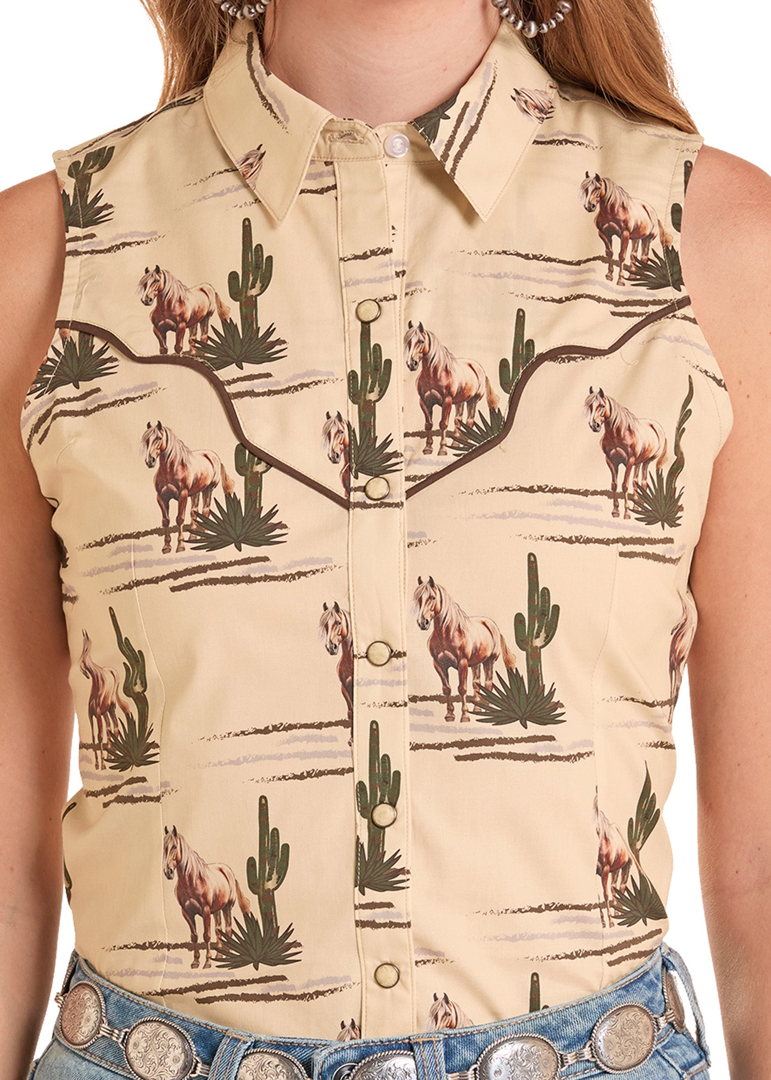 Woman wearing a sleeveless shirt with a cowboy pattern featuring horses and cacti.