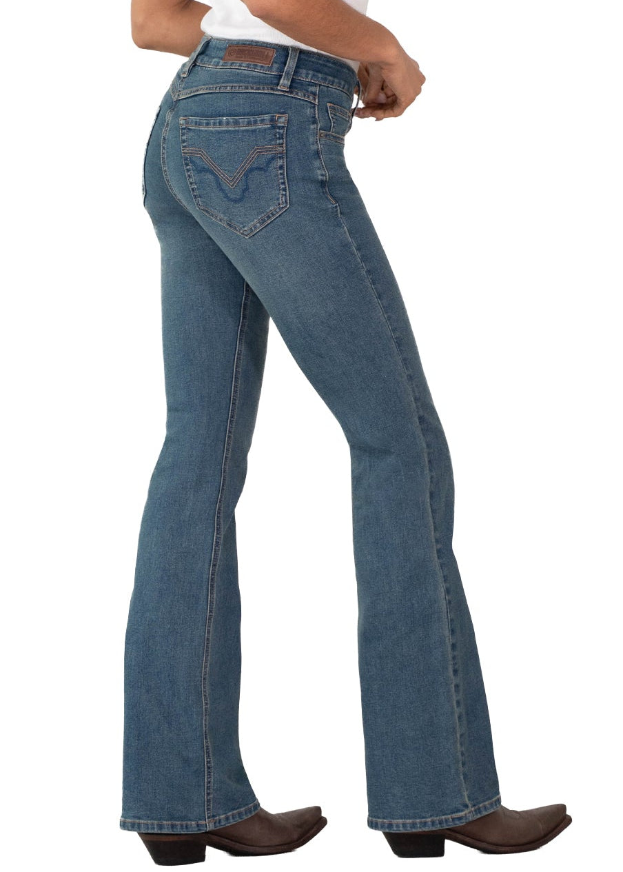A woman modeling a pair of medium-wash blue flare jeans, paired with a white tank top and brown boots, shown from a side-back angle against a plain white background.