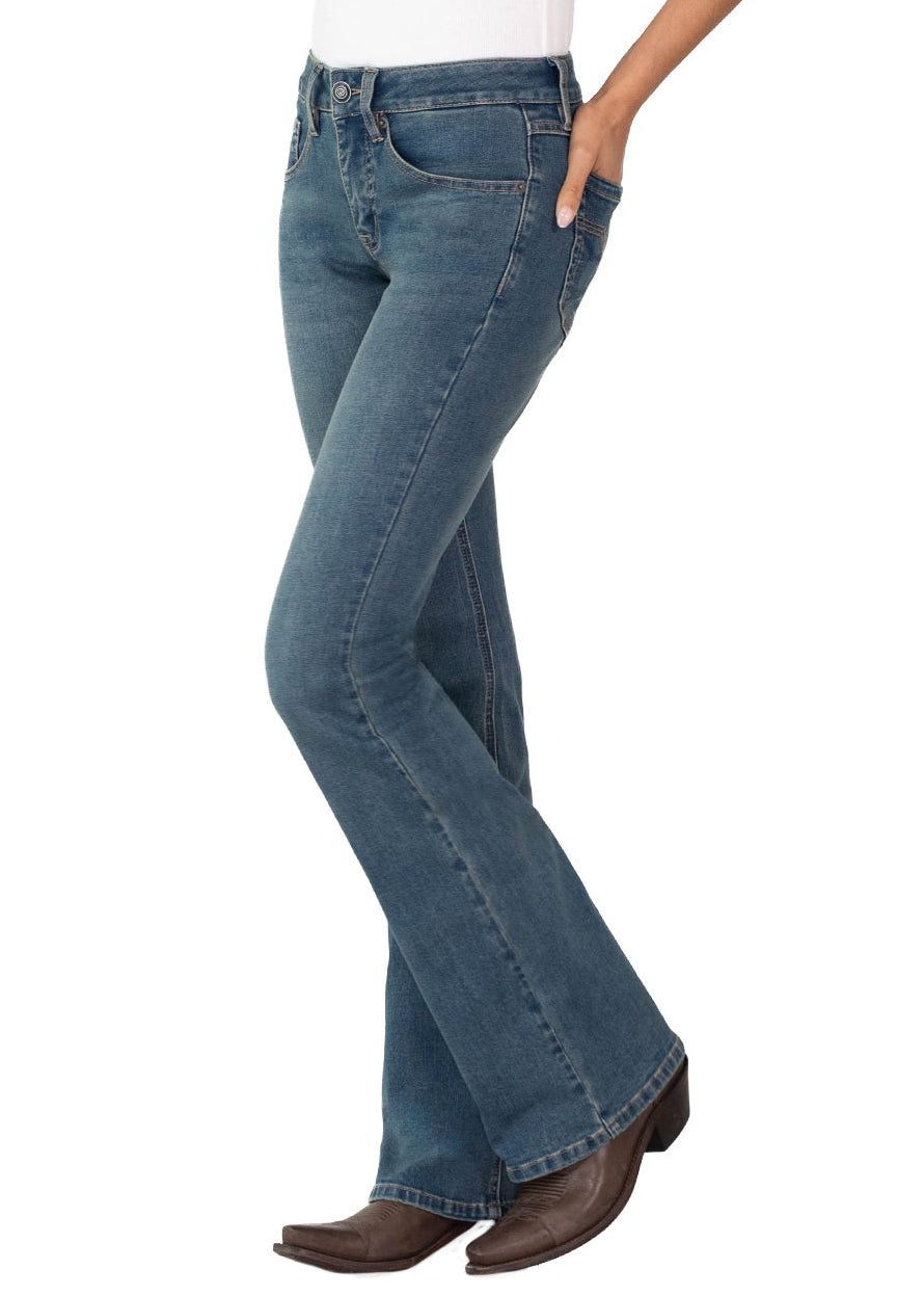 A woman modeling blue flared jeans with a white tank top and brown boots, standing in profile against a plain white background.
