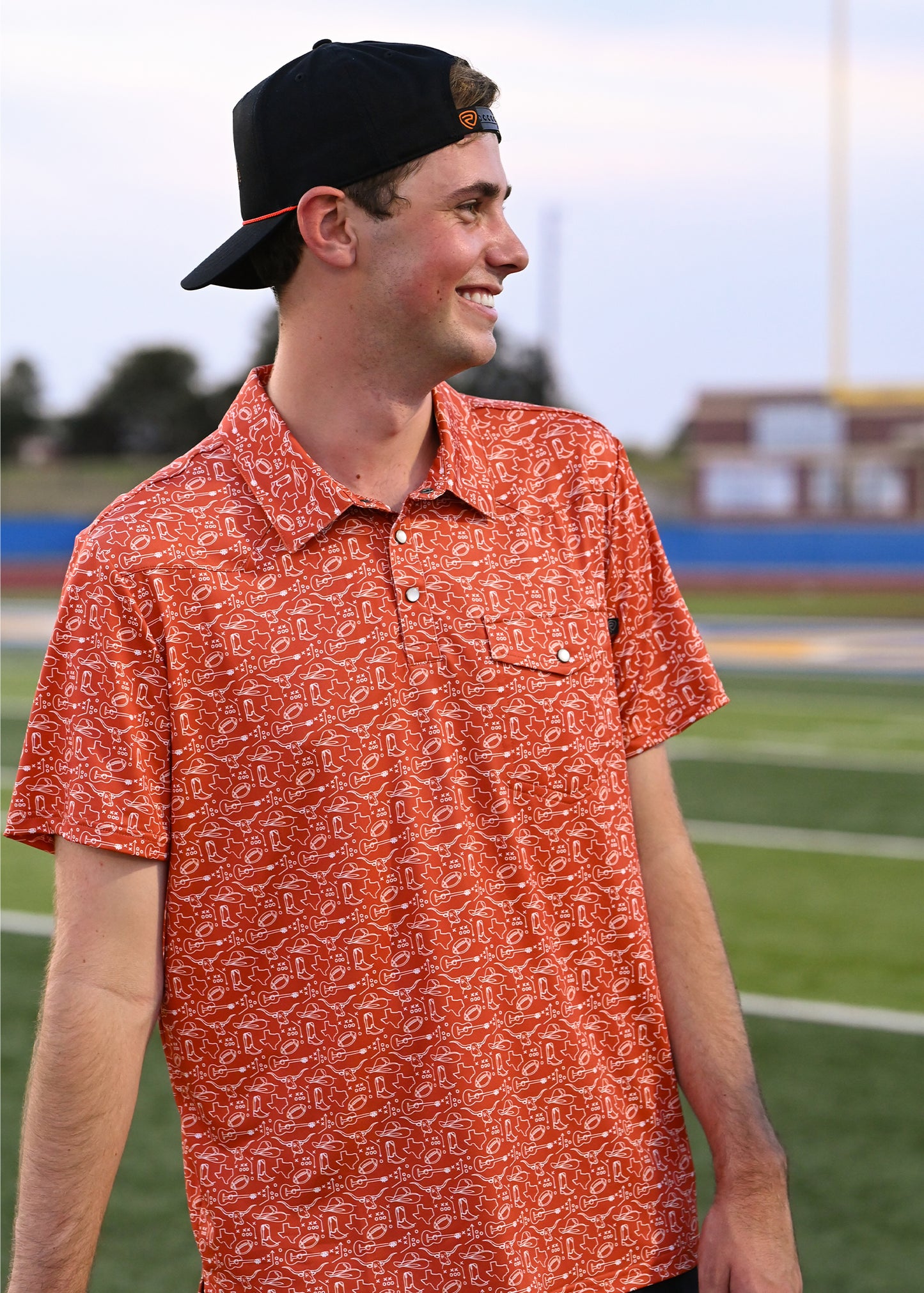 Guy wearing an orange gameday polo and a black cap on a football field