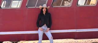Person wearing a cowboy hat and black shirt standing in front of a red train.